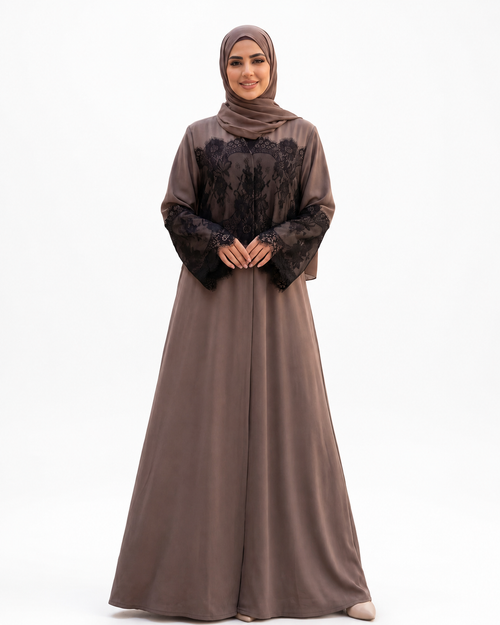 A woman modeling a long taupe-brown abaya dress with black lace sleeves and a matching taupe hijab, standing against a plain white studio background.