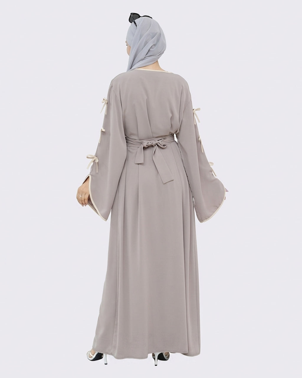 Woman wearing a long, light gray dress with tassel sleeves on a white background