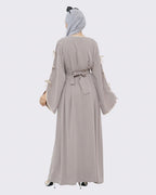 Woman wearing a long, light gray dress with tassel sleeves on a white background