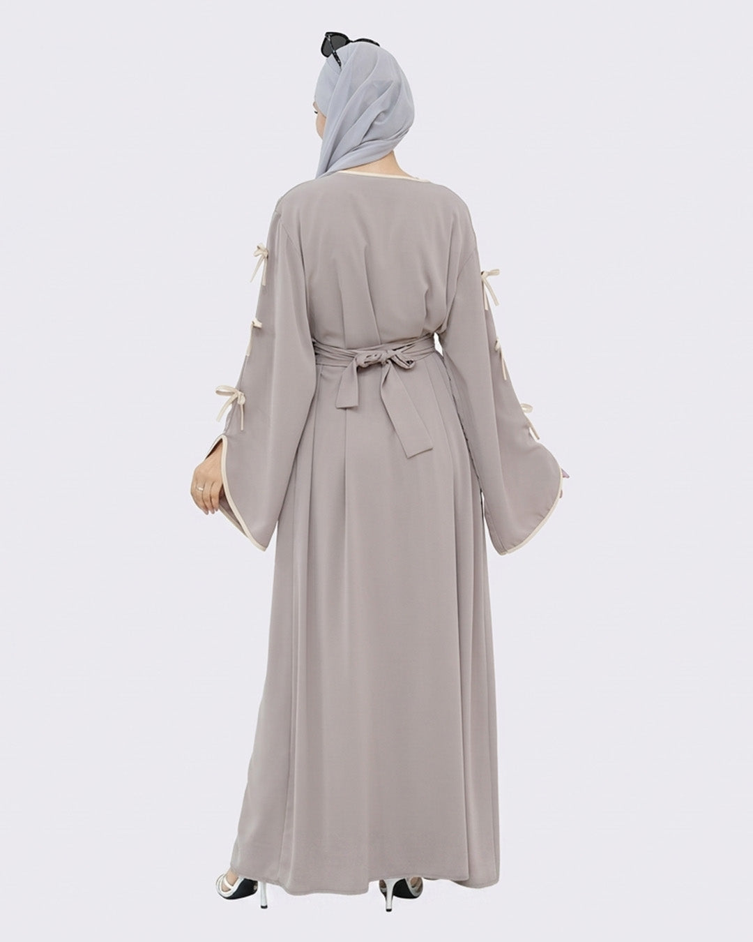 Woman wearing a long, light gray dress with tassel sleeves on a white background